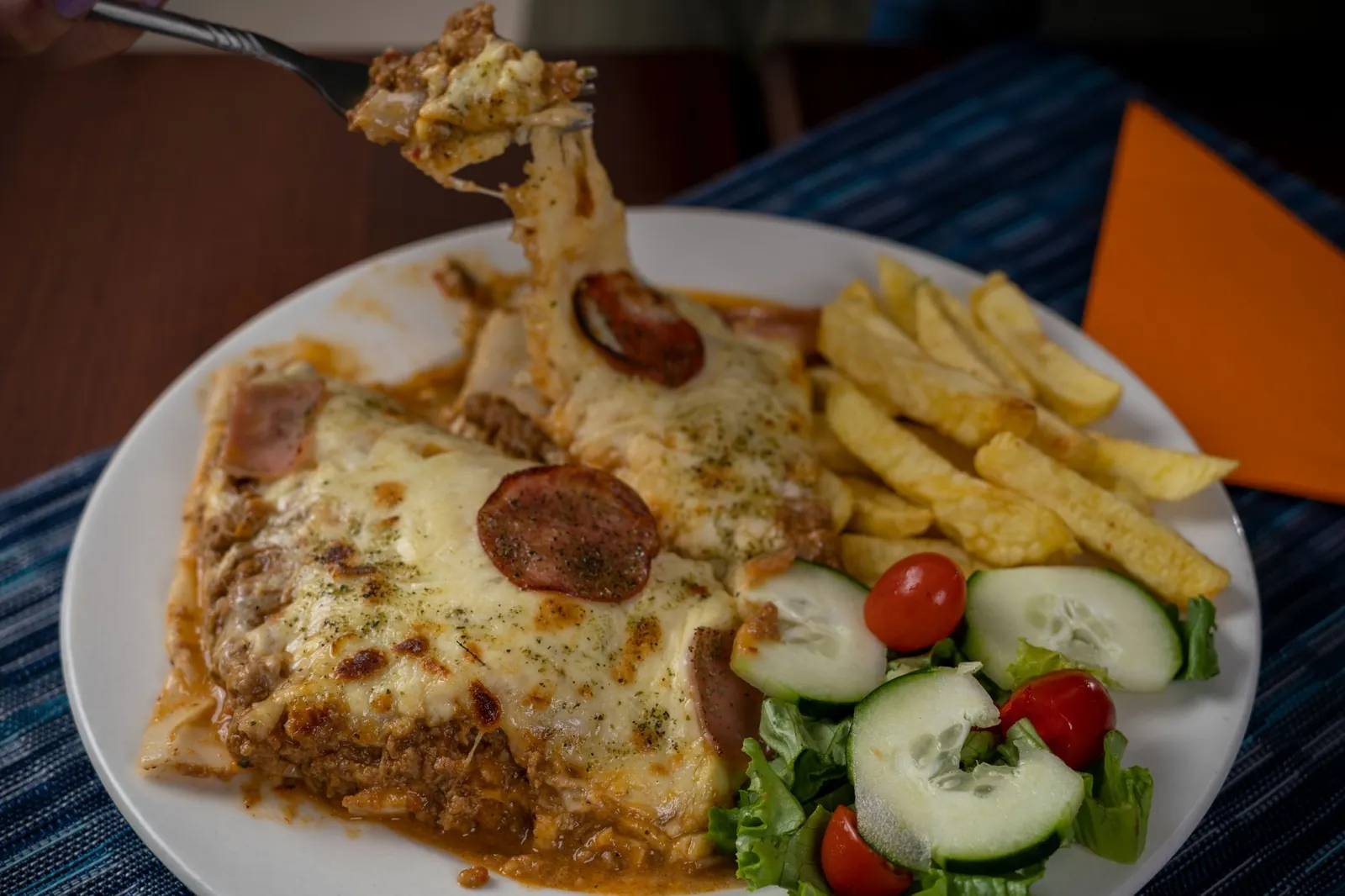 Lasaña con queso derretido, papas fritas y ensalada